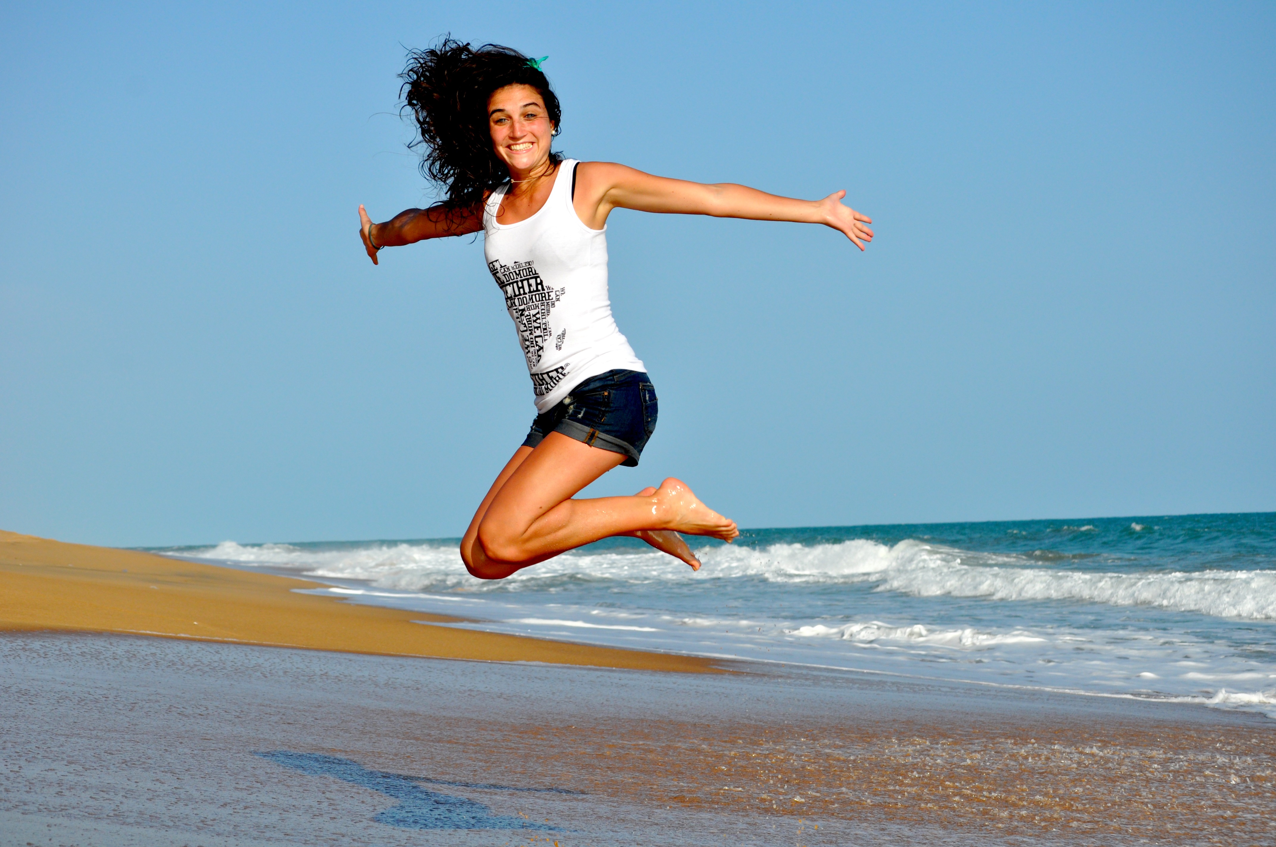 Junge Frau, die am Meer in die Luft springt